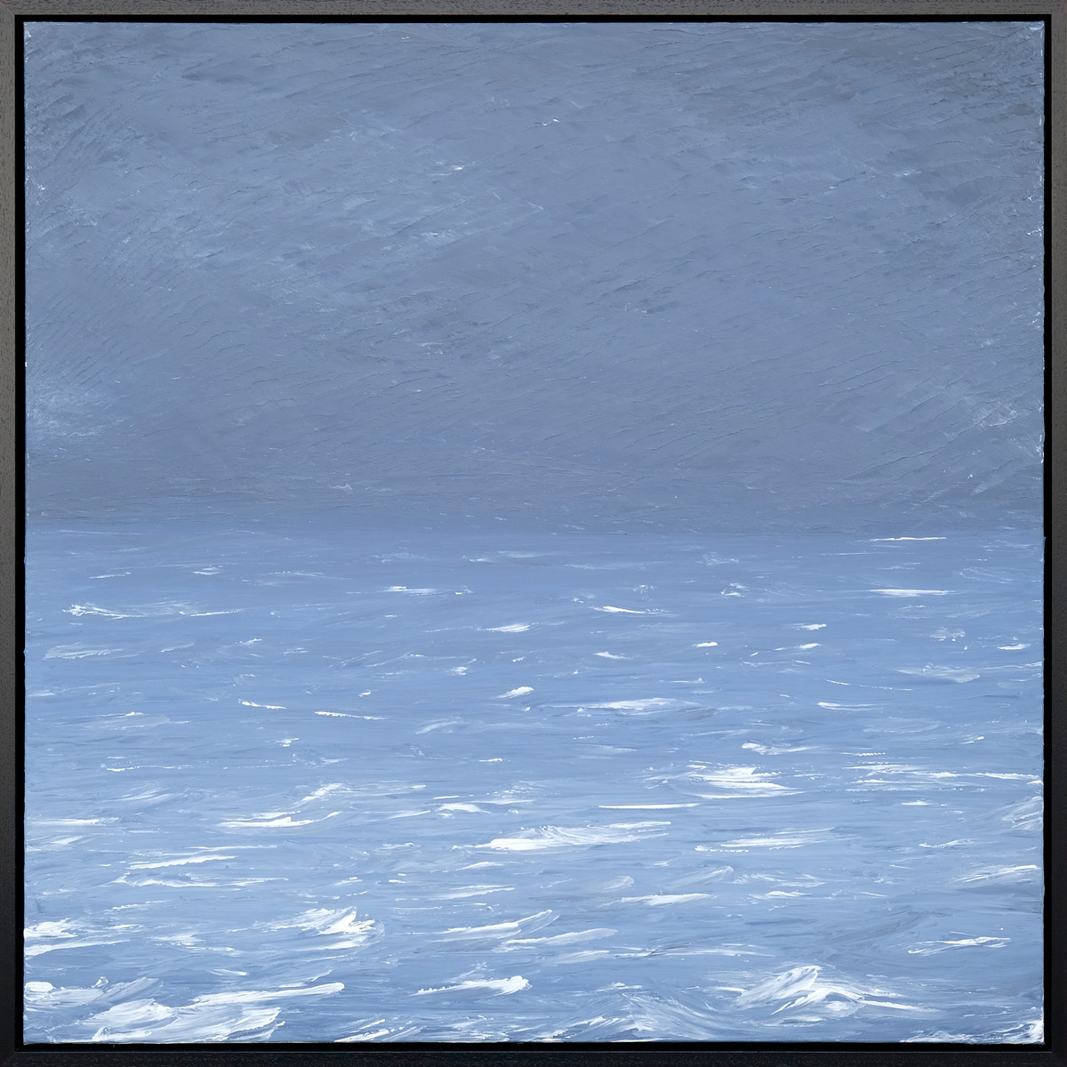 A pale blue sea and textured sky meet at a faint horizon, with bright white wave crests across the foreground in a black frame.
