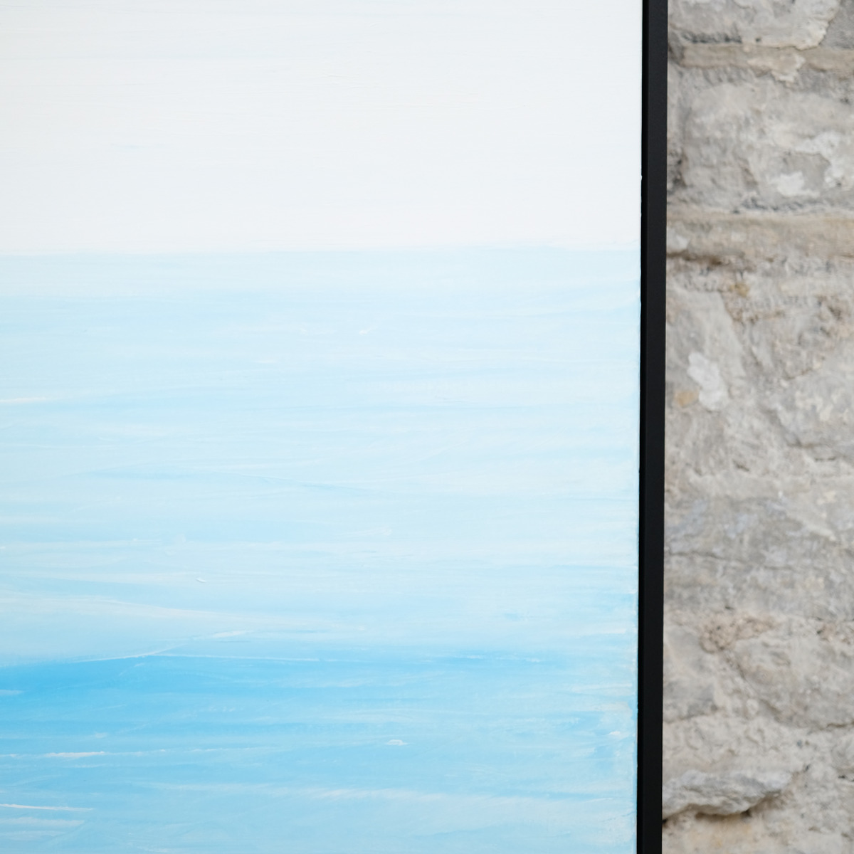 Detail of Pale Distance showing a pale sky above light blue water, soft white horizontal marks and brighter blue paint beside the right edge of the black frame.
