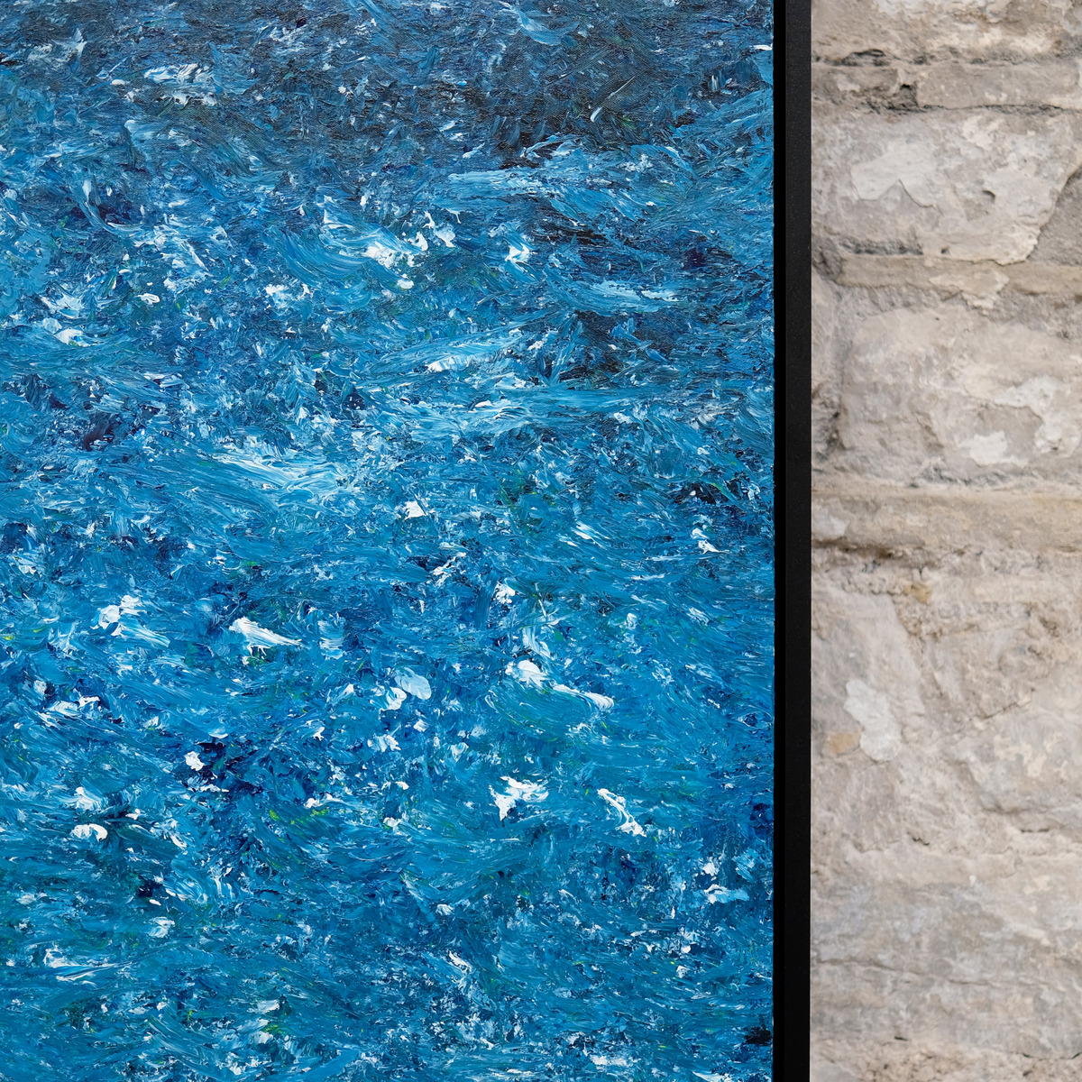 Detail of A Thousand Tides showing densely layered bright blue and turquoise paint, dark blue marks and raised white strokes beside the right edge of the black frame.
