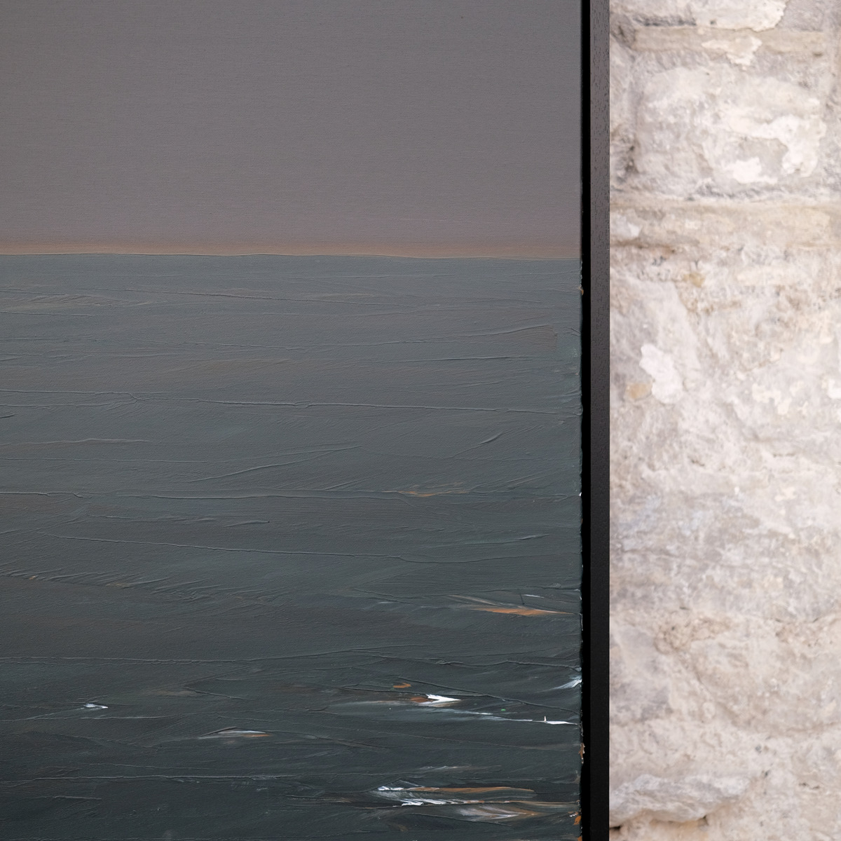 Detail of The Quiet Line showing a narrow warm horizon between grey-violet sky and blue-green water, with pale and ochre marks beside the right edge of the black frame.