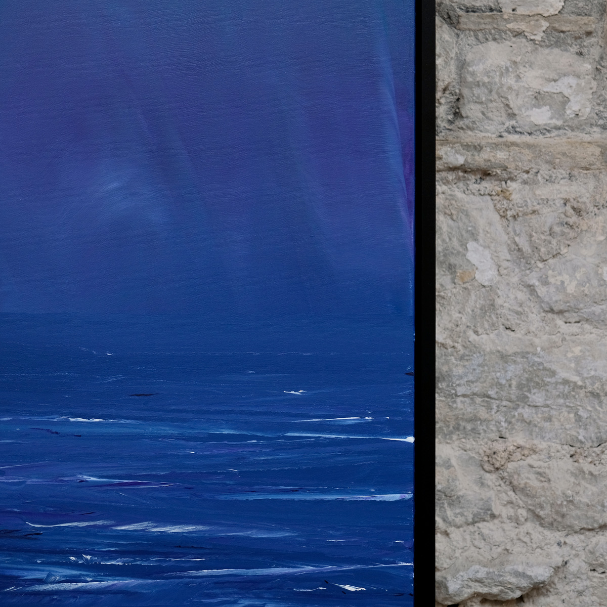 Detail of The Long Blue showing deep blue sky above a low horizon, pale sweeping marks and white wave strokes beside the right edge of the black frame.