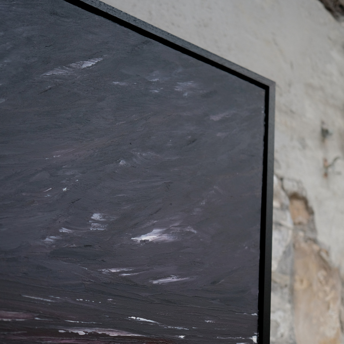 Angled close-up of the upper-right corner of The Sea Unquiet, showing pale diagonal marks across a dark grey painted sky and the black frame.