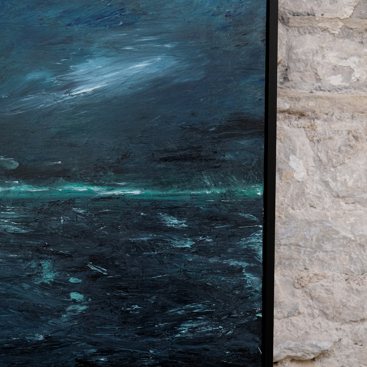 Detail of A Thread of Light showing a dark blue-grey sky, a narrow turquoise-green horizon and pale marks across dark water beside the right edge of the black frame.