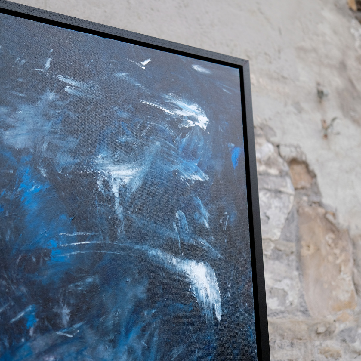 Angled close-up of the upper-right corner of Wildwater, showing blue-grey paint, pale sweeping marks, canvas texture and the black frame.