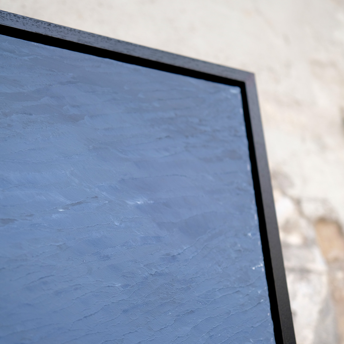 Angled close-up of the upper-right corner of Silver Unrest, showing textured pale blue paint and the black frame.